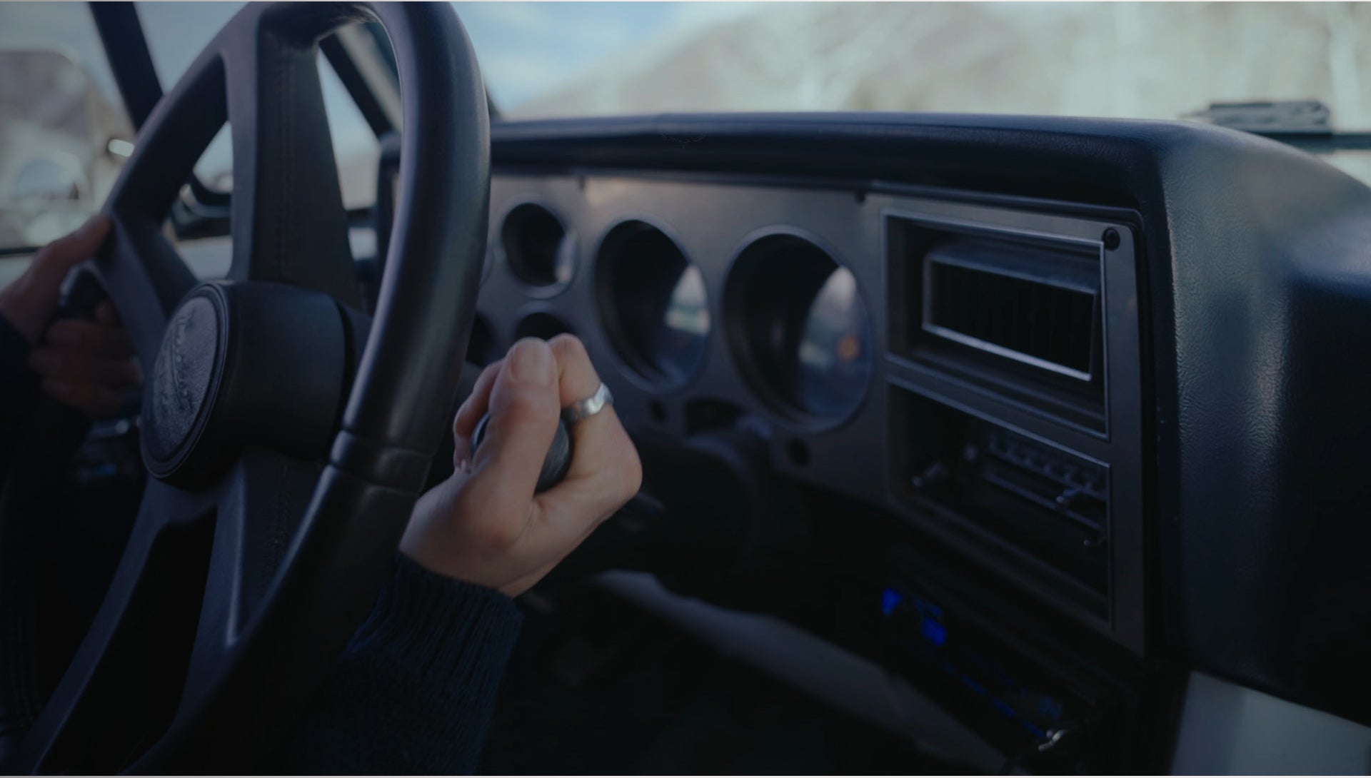Close-up of a person's hand on a car steering wheel with dashboard details.
