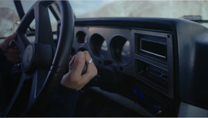 Close-up of a person's hand on a car steering wheel with dashboard details.