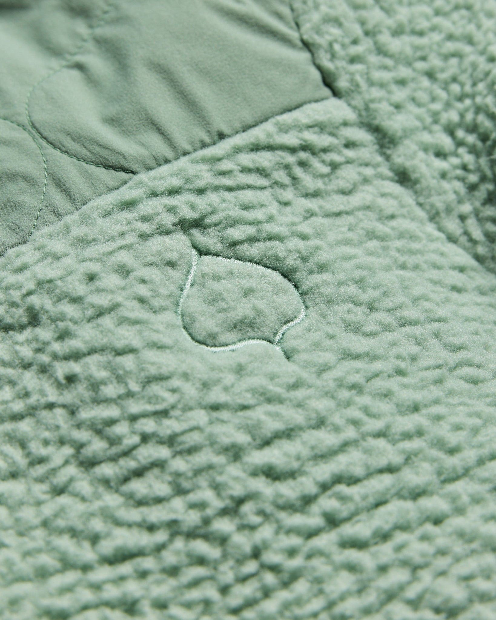 A quilted fabric with a leafy pattern in soft green tones creates a plush texture, ideal for cozy settings.