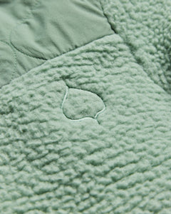 A quilted fabric with a leafy pattern in soft green tones creates a plush texture, ideal for cozy settings.