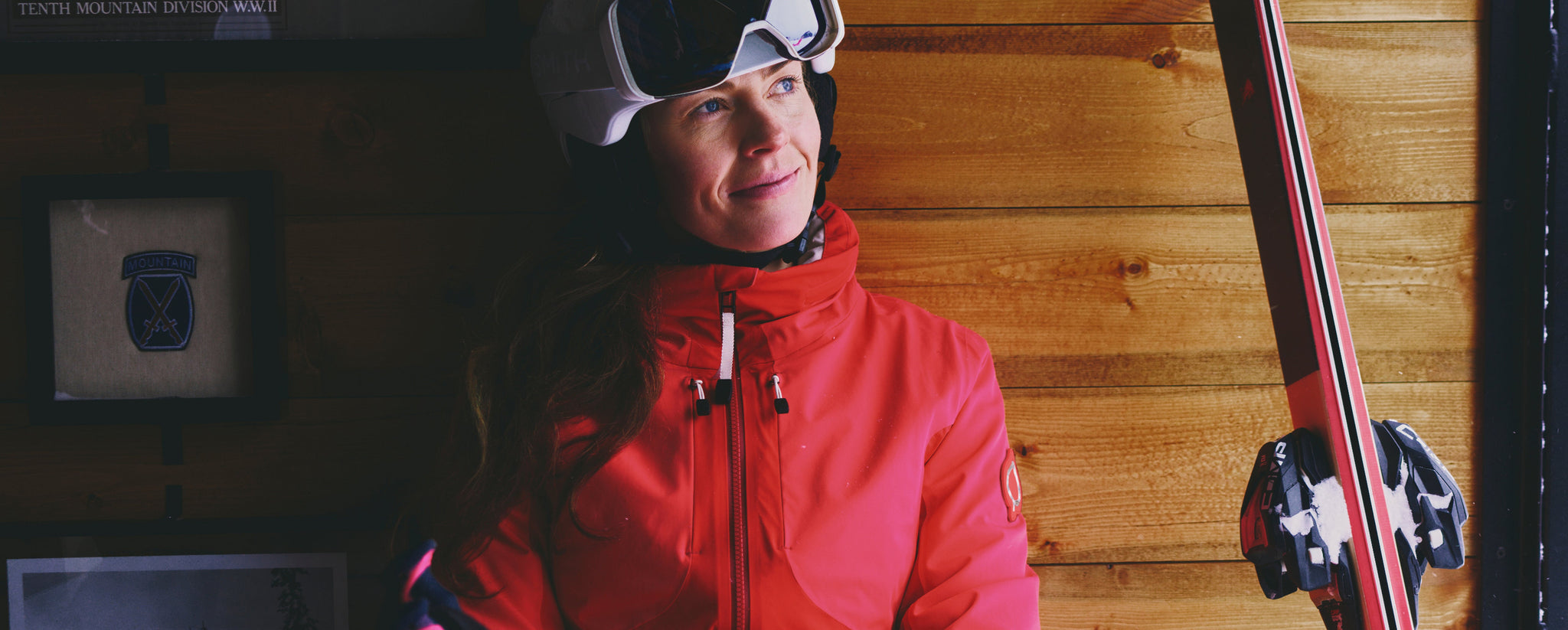 Person in red ski jacket with skis leaning against a wooden wall