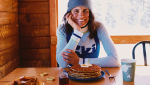 Woman sitting at a table with pancakes and a coffee cup, smiling.