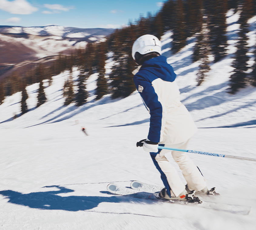 Person skiing down a snowy slope with trees and mountains in the background
