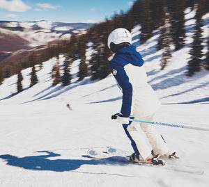 Person skiing down a snowy slope with trees and mountains in the background