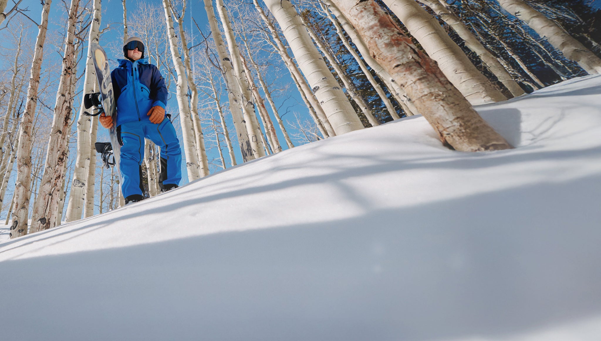 Person in blue snowsuit standing on a snowy slope with trees in the background