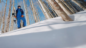 Person in blue snowsuit standing on a snowy slope with trees in the background