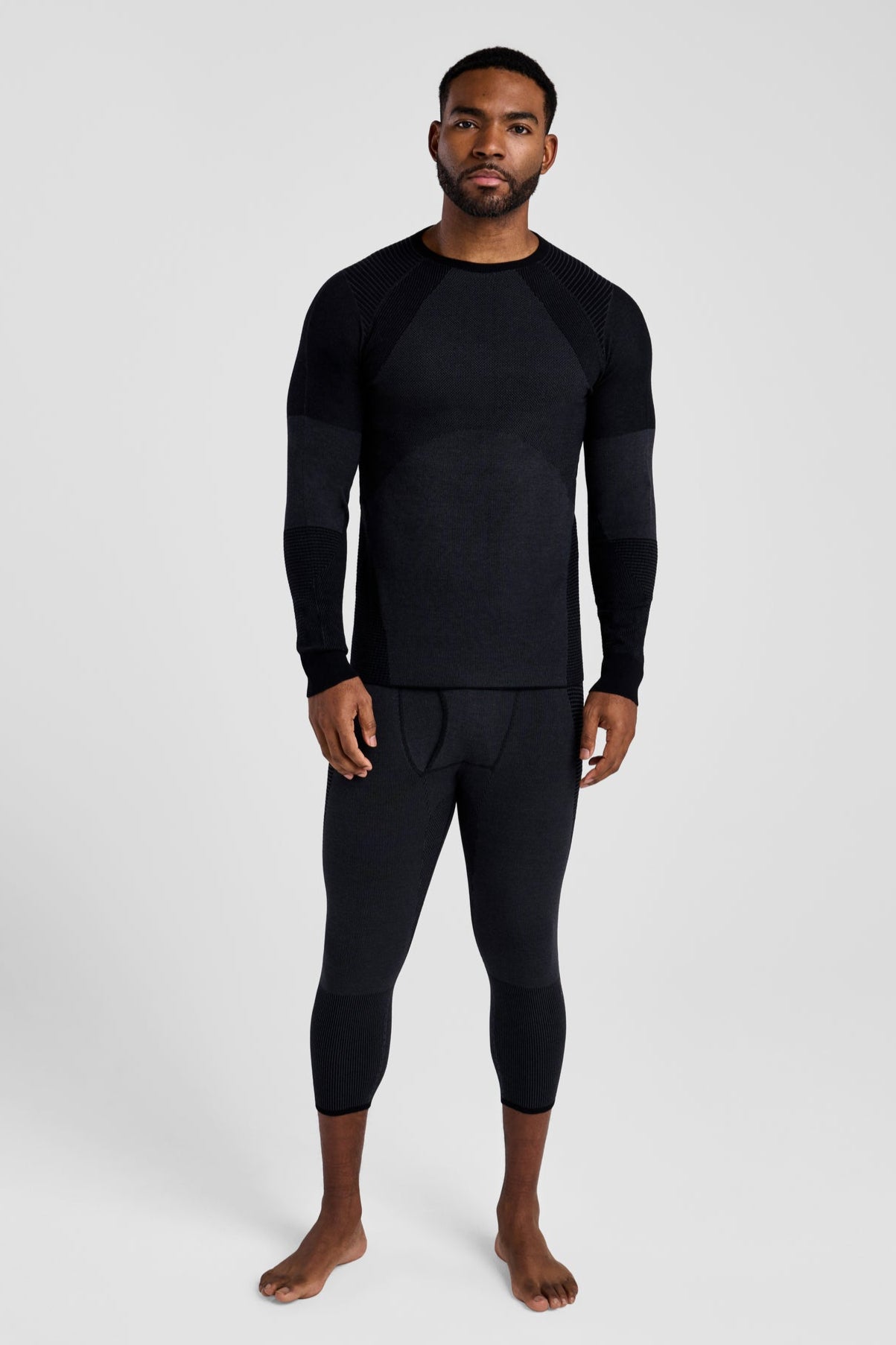 Man wearing a black long-sleeve top and black leggings on a white background