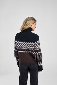 Woman wearing a patterned sweater and dark pants on a white background