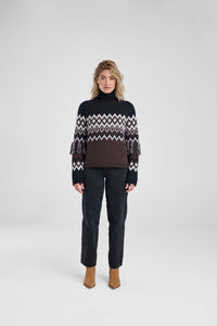 Woman wearing a patterned sweater and dark pants on a white background
