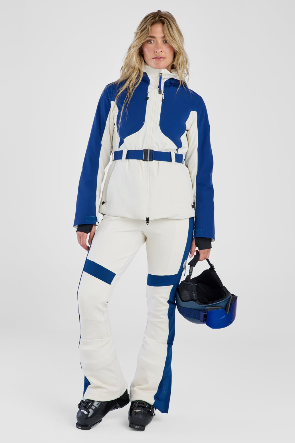 Person wearing a blue and white ski suit holding a helmet on a white background