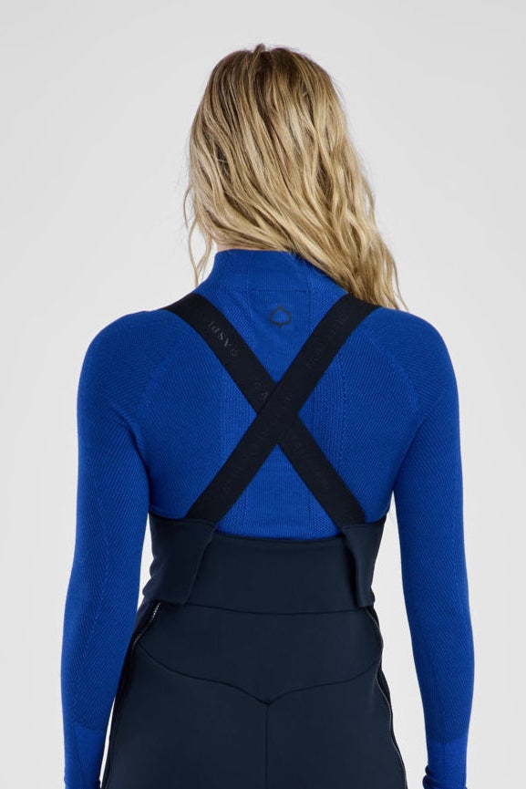 Person wearing a blue top and black bib overalls on a white background