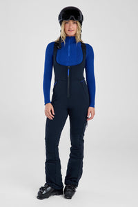 Person wearing a blue top and black snow bib with a helmet on a white background