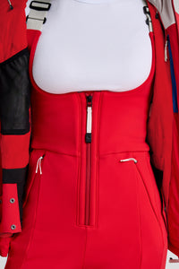 Red ski bib with a white shirt underneath, surrounded by other winter clothing.