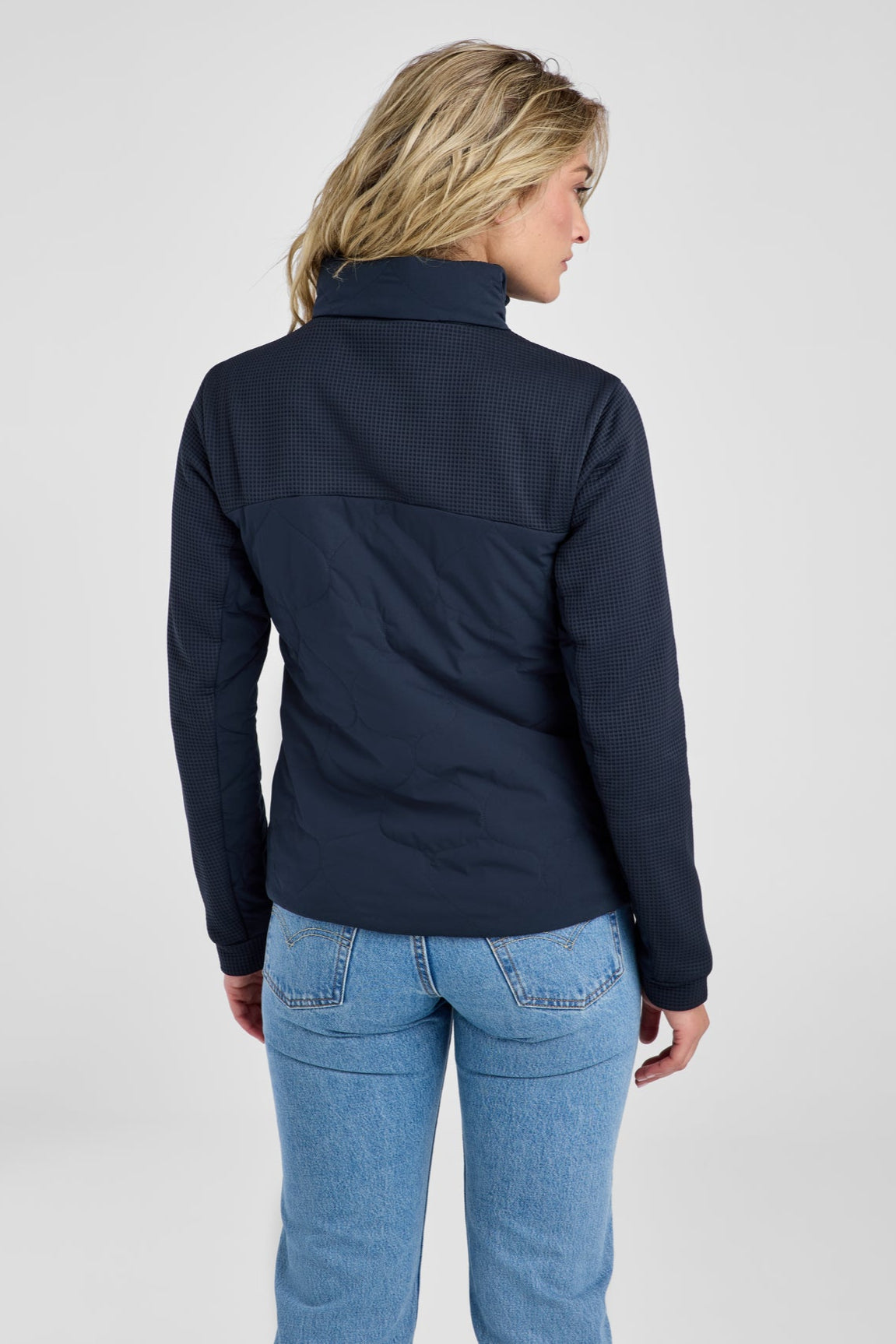 Person wearing a navy jacket and blue jeans on a gray background