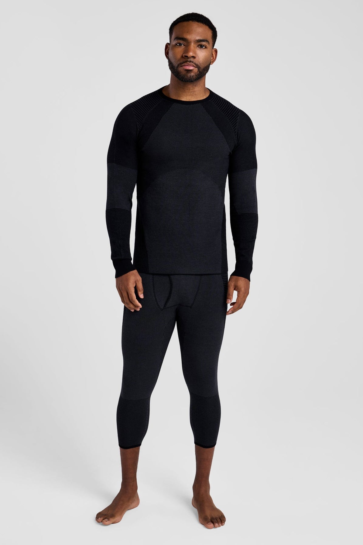 Man wearing a black long-sleeve top and black leggings on a white background