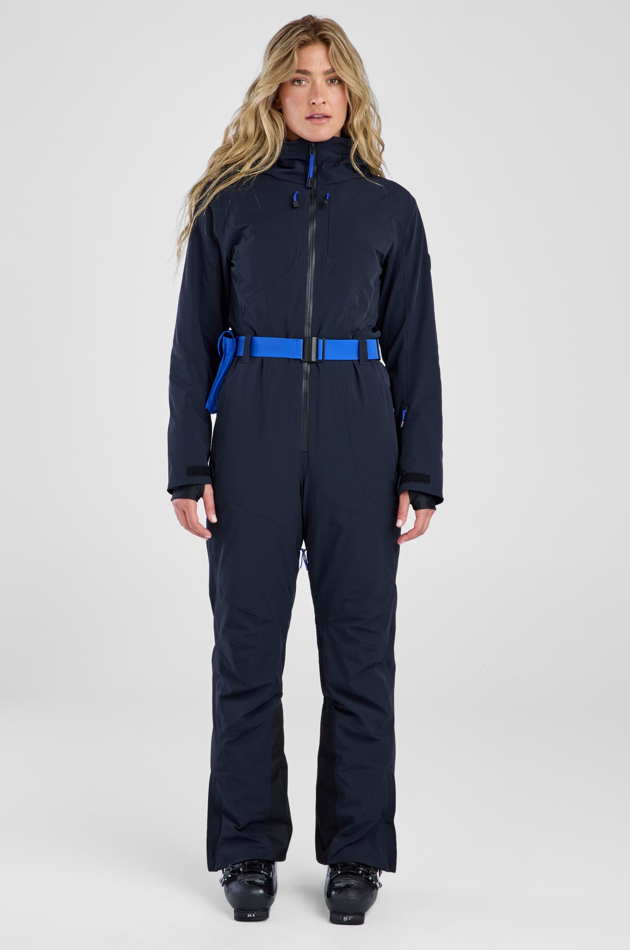 Woman wearing a navy blue ski suit with a blue waistband on a white background