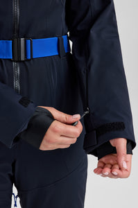 Person wearing a dark blue snowsuit with a blue belt on a light gray background