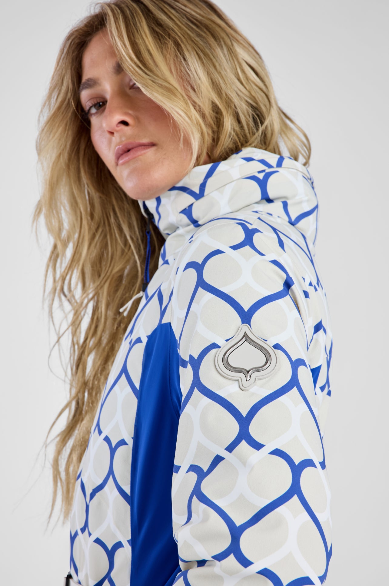 Person wearing a white and blue patterned jacket with a brand logo on a white background