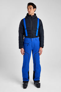 Person wearing a black and blue winter outfit with suspenders on a white background