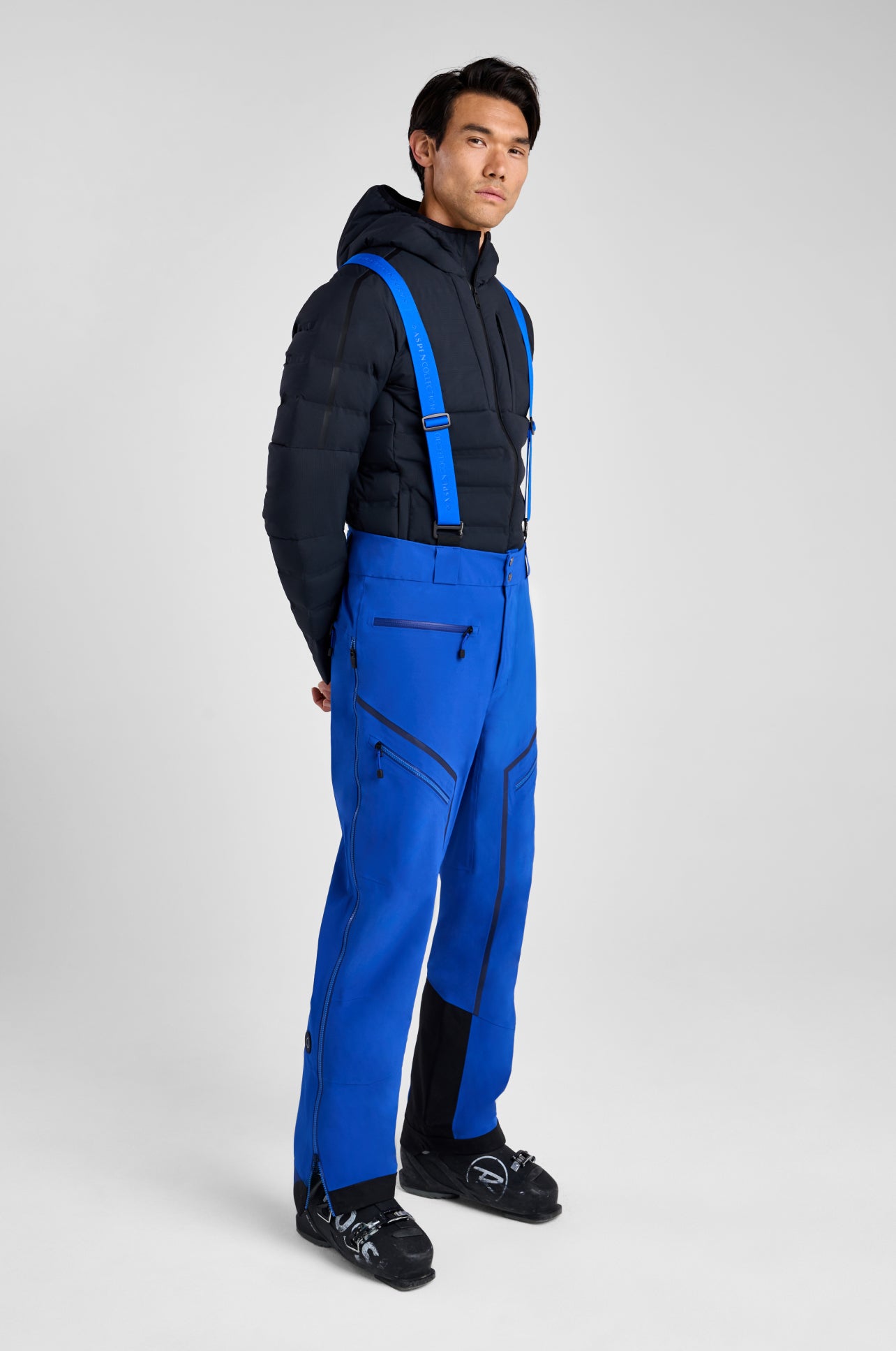 Person wearing a black jacket and blue pants with suspenders on a white background