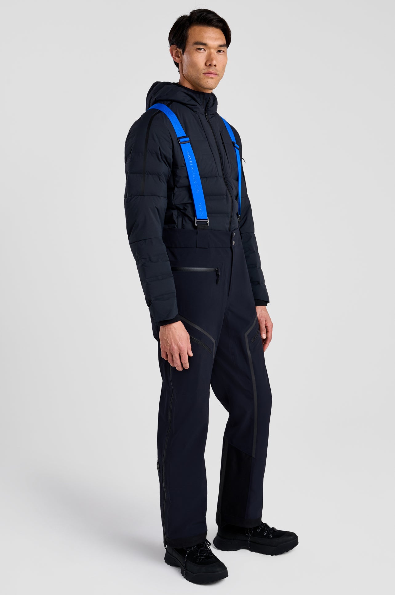 Person wearing a black snowsuit with blue straps on a white background