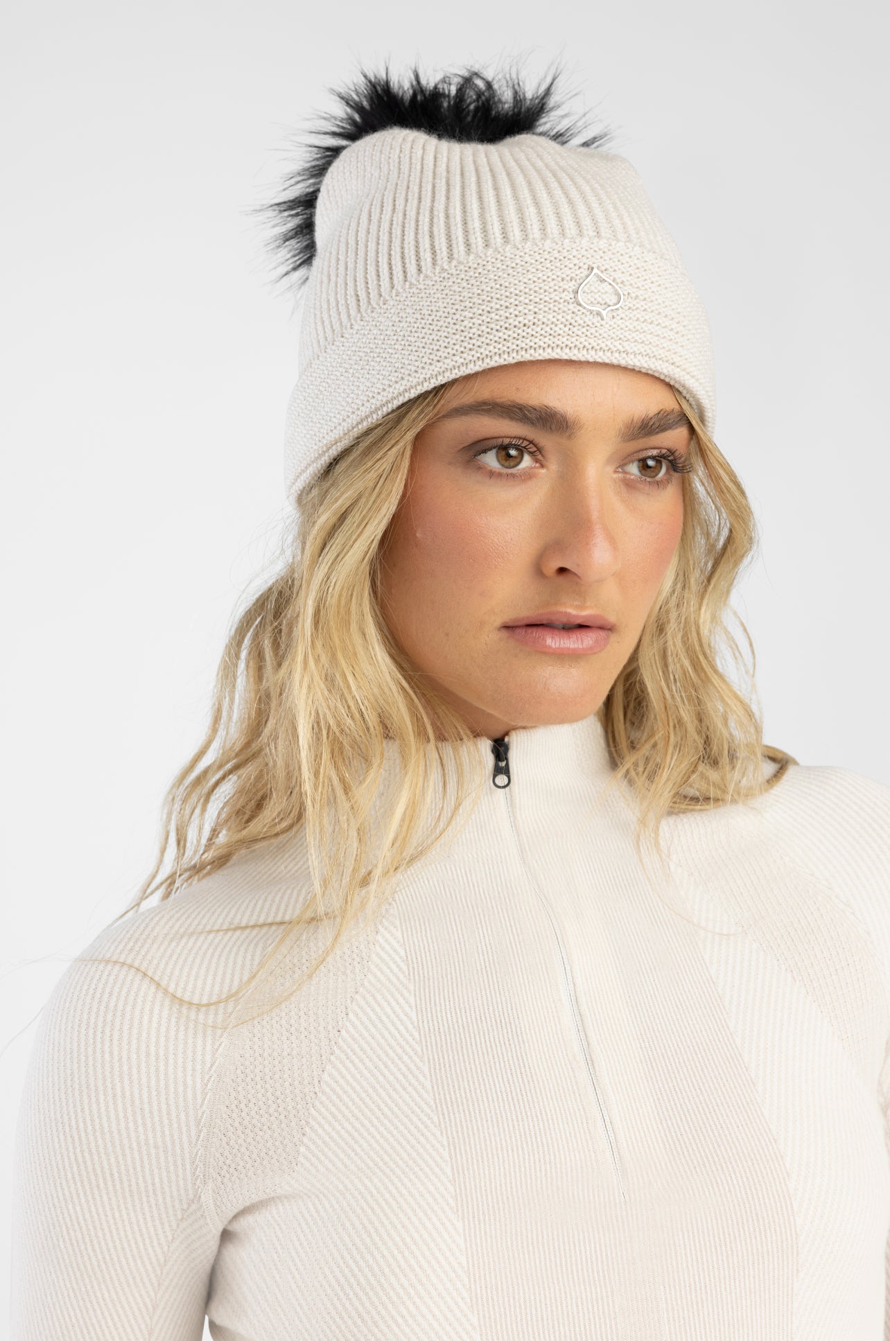 Woman wearing a white knit beanie with a black pom-pom on a white background