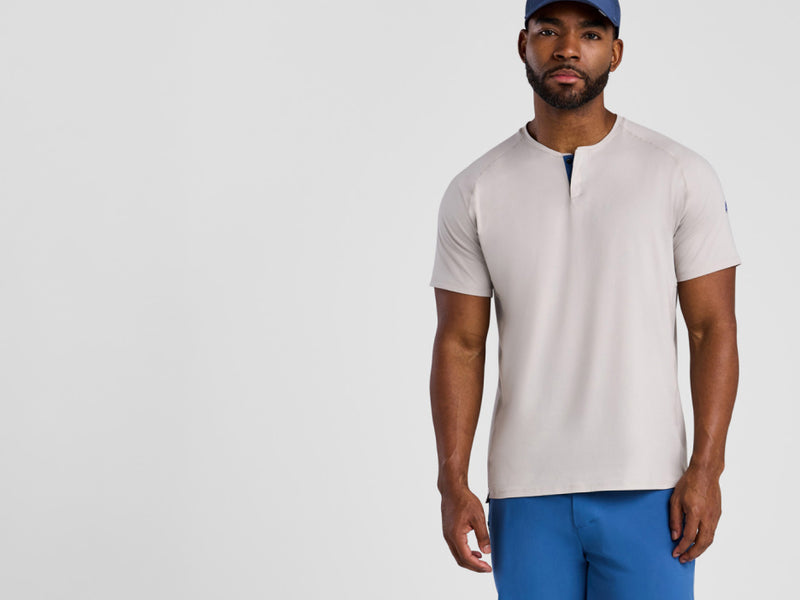 Man wearing a beige henley shirt and blue pants on a light gray background