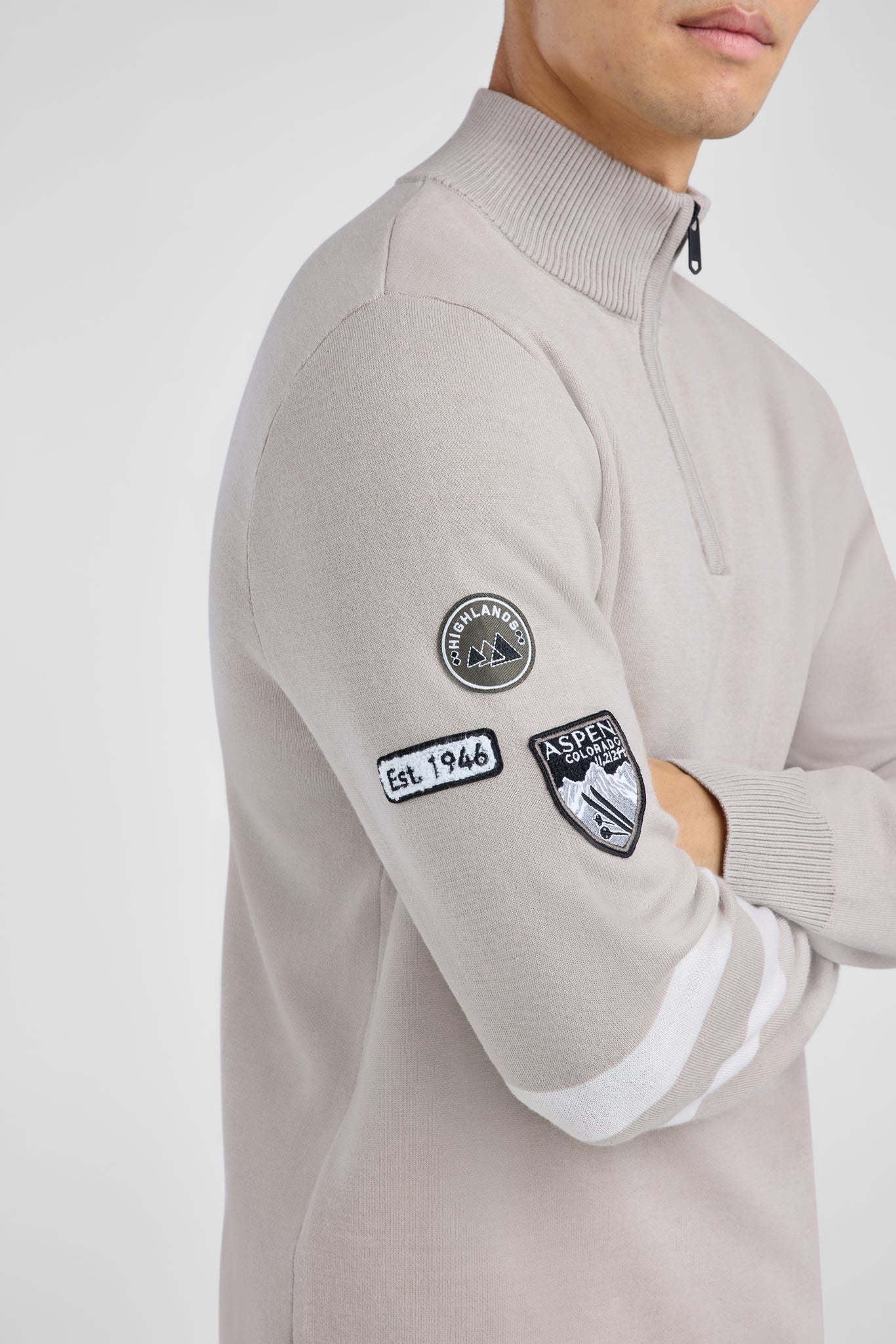 Person wearing a light gray sweater with patches on a white background