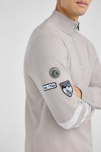 Person wearing a light gray sweater with patches on a white background