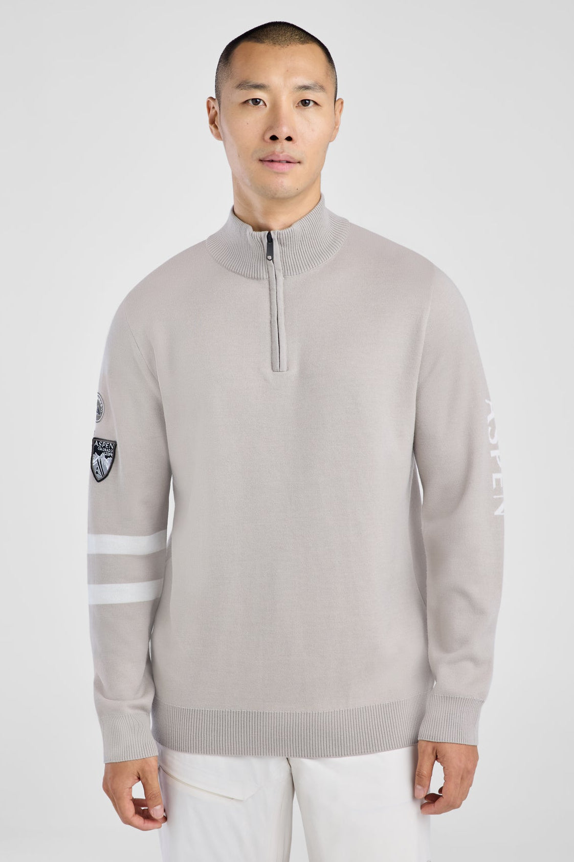 Man wearing a light gray sweater with white pants on a white background