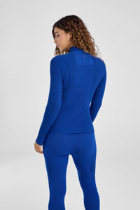 Woman wearing a blue baselayer outfit on a light gray background
