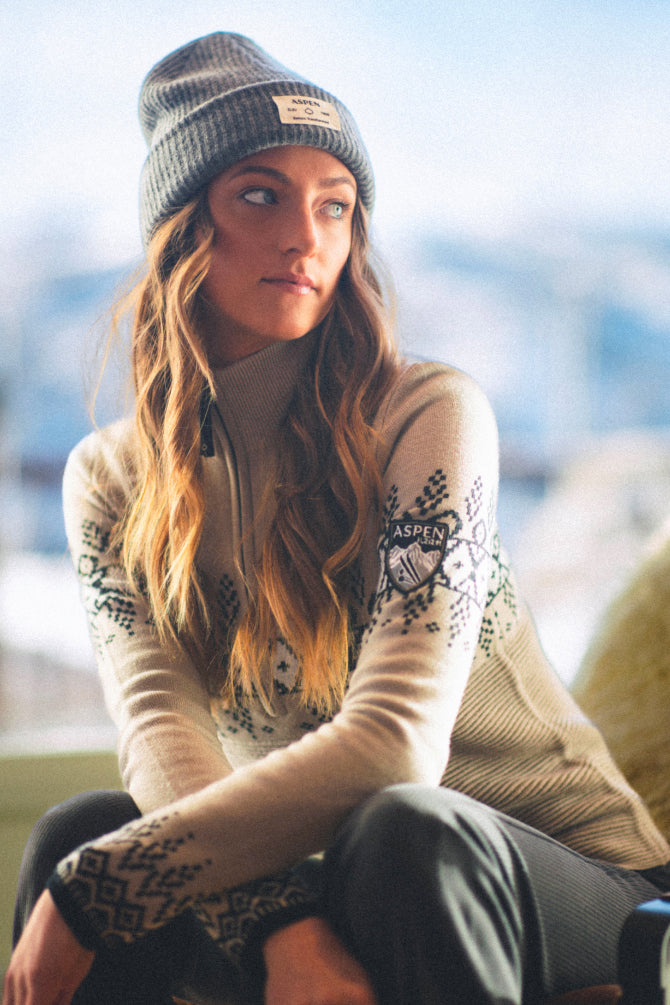 Woman wearing a patterned sweater and beanie with a blurred outdoor background
