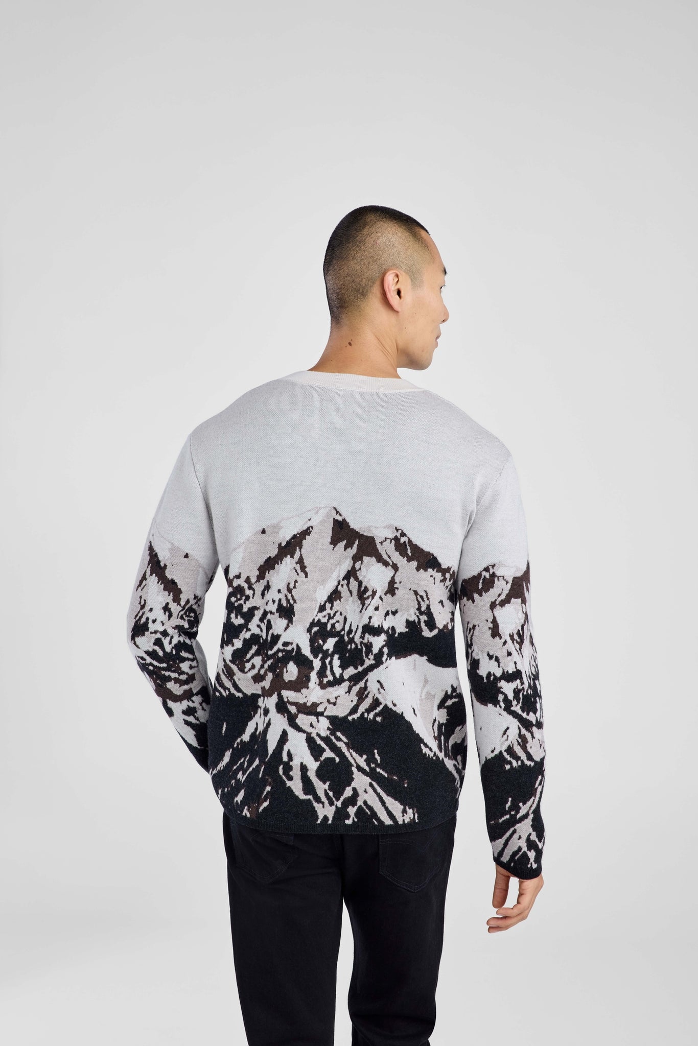 Man wearing a sweater with black abstract mountain pattern on a plain background