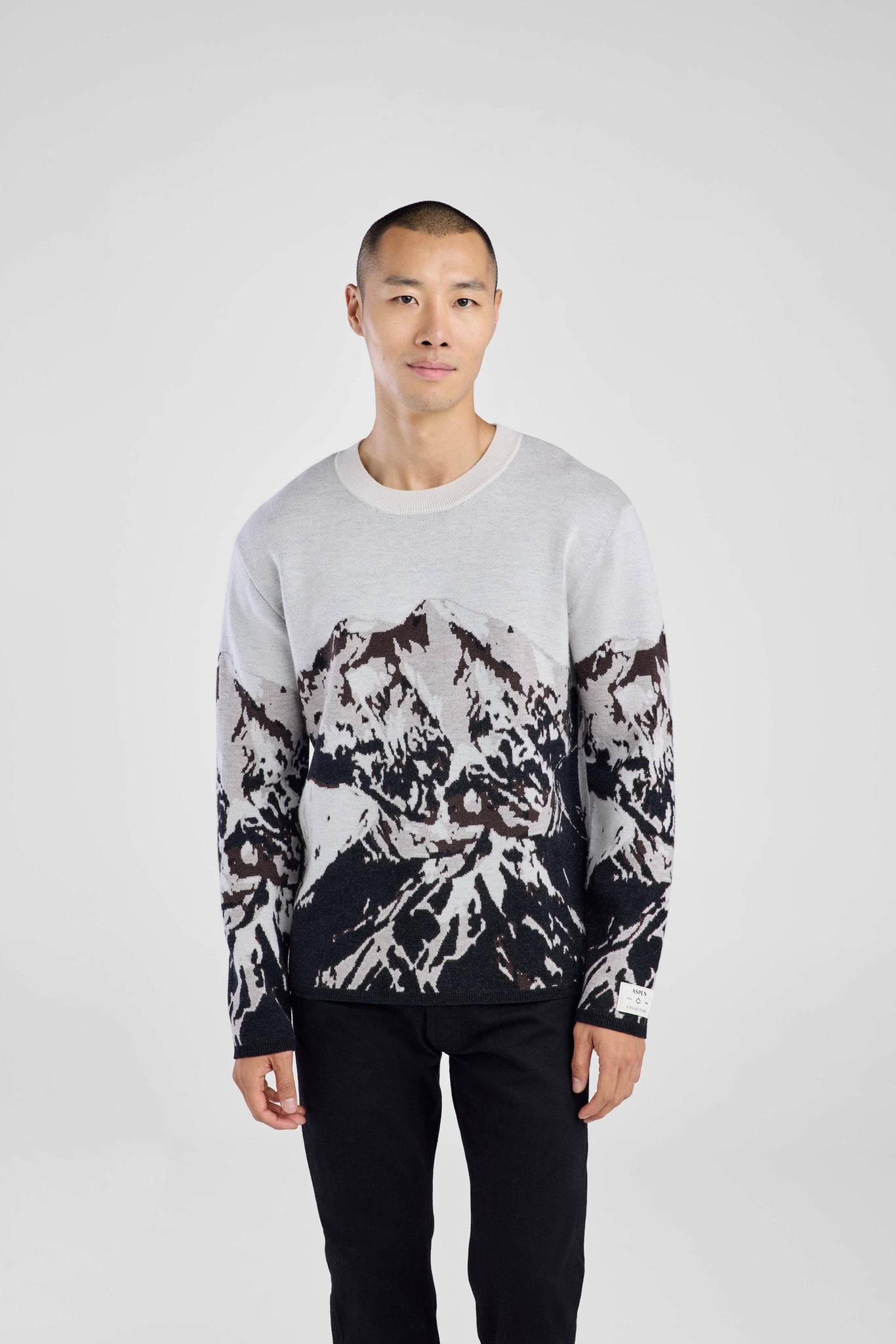 Man wearing a sweater with black abstract mountain pattern on a plain background