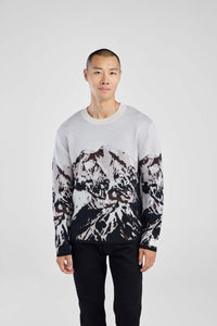 Man wearing a sweater with black abstract mountain pattern on a plain background