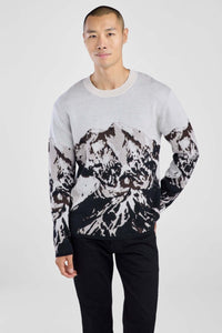 Man wearing a sweater with black abstract mountain pattern on a plain background