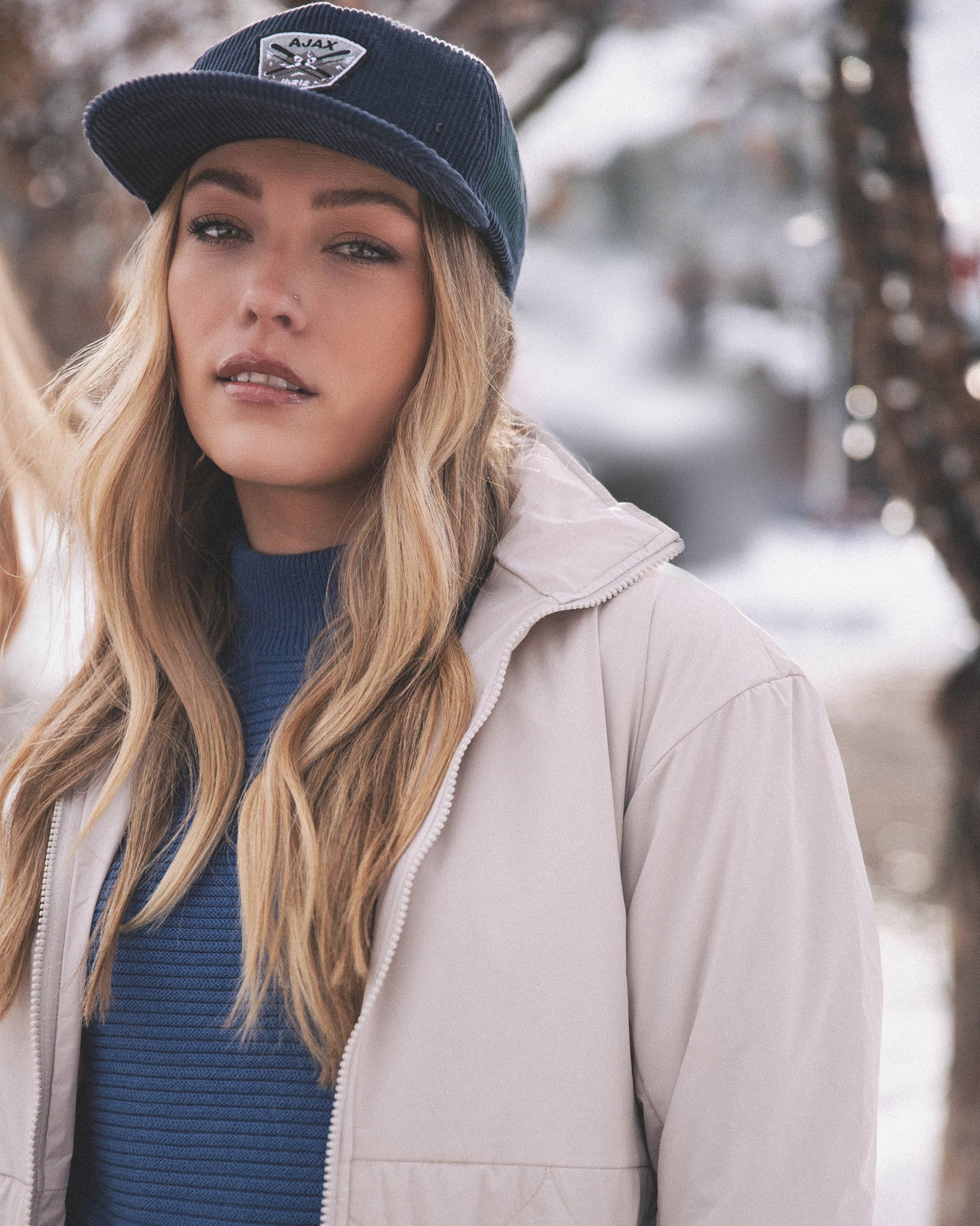 Woman looks at camera in her white aspen collection jacket, zipped open, with a blue sweater beneath it and a 