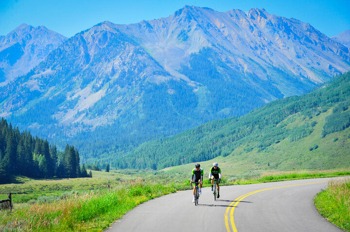 Two cyclists on a winding road with mountains in the background