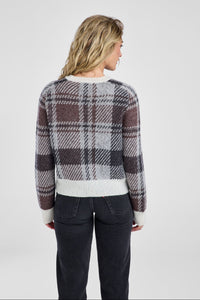 Woman wearing a plaid sweater and dark pants on a white background
