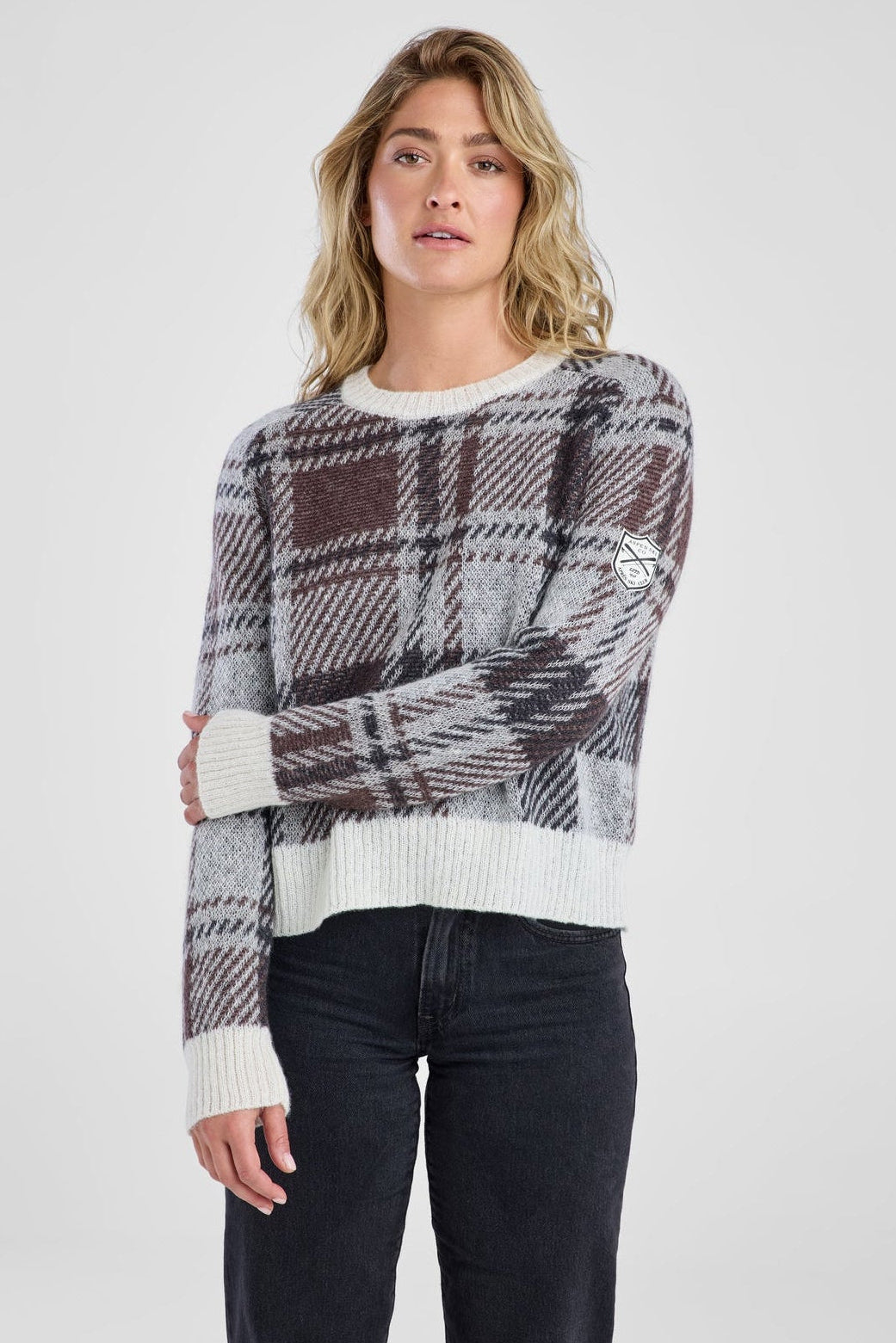 Woman wearing a plaid sweater over a white shirt with black pants on a white background