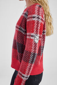 Side view of a woman wearing a red plaid sweater with white detail patch