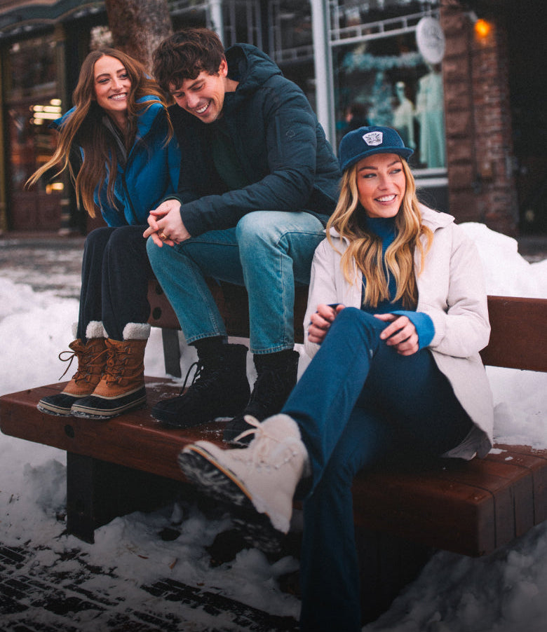 Three people sitting on a bench in a snowy outdoor setting