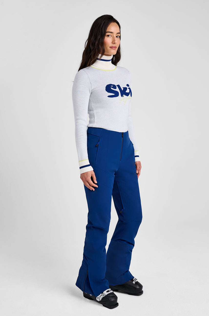 Person wearing a white turtleneck with a logo and blue pants on a white background